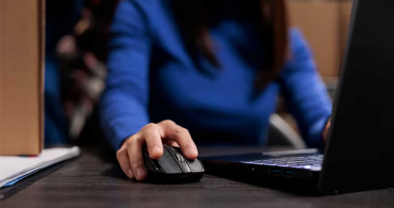 O persoană verificând compartimentul bateriilor și senzorul optic de pe spatele unui mouse wireless