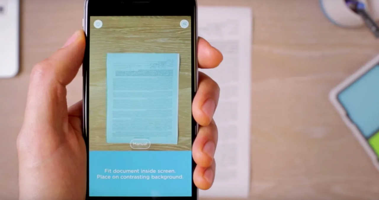 O persoană folosind telefonul mobil pentru a scana un contract pe birou prin aplicația Google Drive